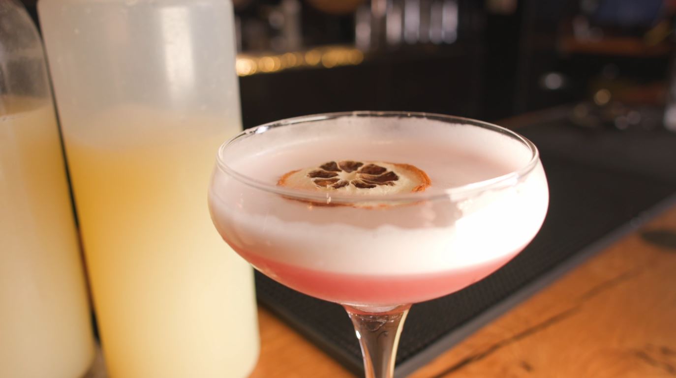 A pink-colored cocktail with a dried orange floating on top