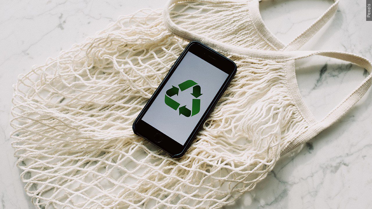 A reusable grocery bag and phone with the recycle symbol on it