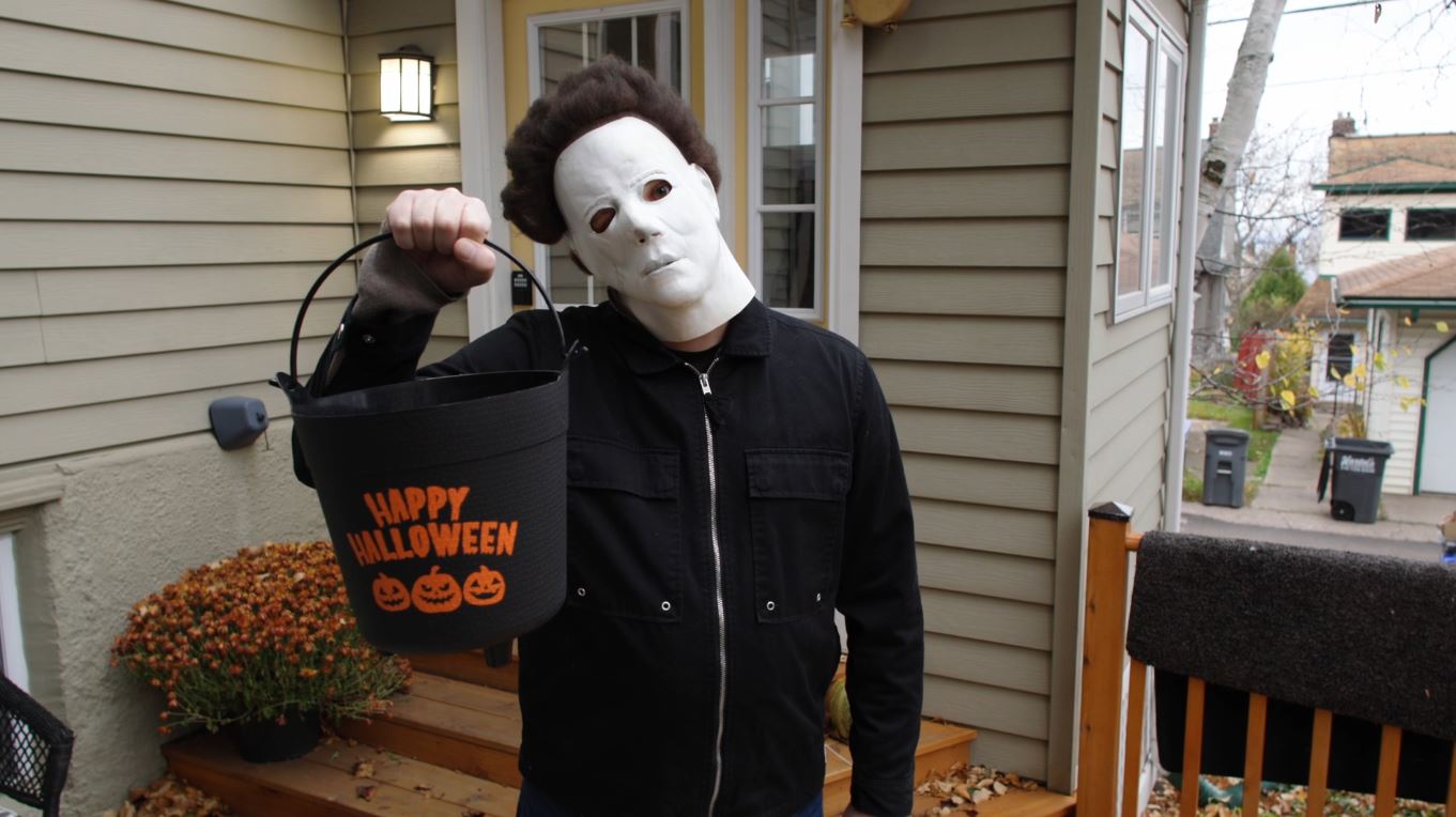 A man in a Michael Myers mask with a bucket that says "Happy Halloween"